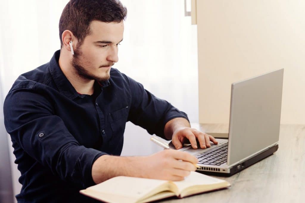 Un hombre estudiando para sus oposiciones de educación física con un ordenador portátil y un cuaderno.