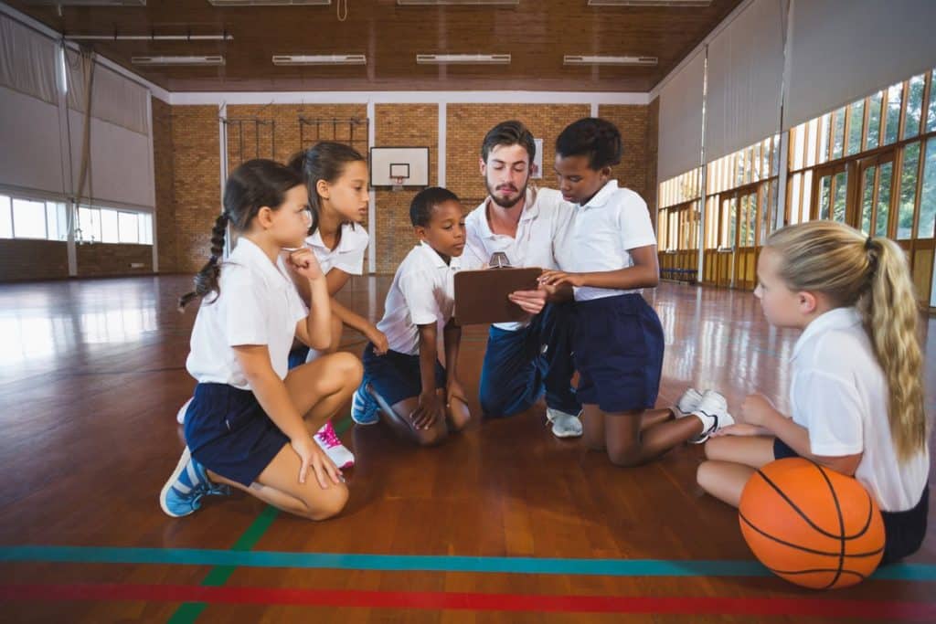 Un grupo de alumnos alrededor de su profesor de educación física repasando juntos.