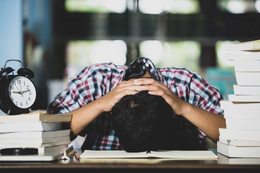 Hombre con la cabeza apoyada sobre un libro abierto cansado de estudiar